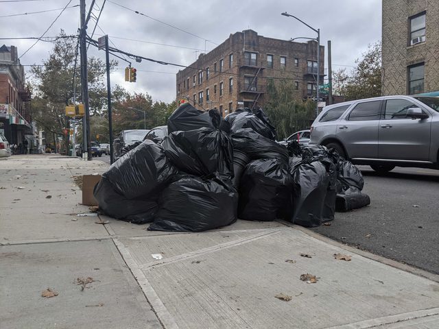 A pile of trash bags sits on a city sidewalk.